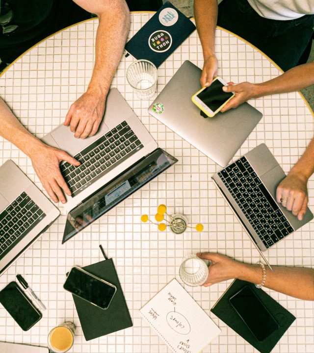 Top view of a team collaborating with laptops, phones, and notes in a modern office.